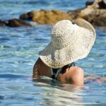 photo de dos d'une femme qui se baigne dans la mer, avec un chapeau de paille