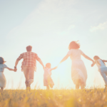 photo d'une famille de 5 personnes qui marche horizontalement en se donnant la main, vers l'horizon ensoleillé.